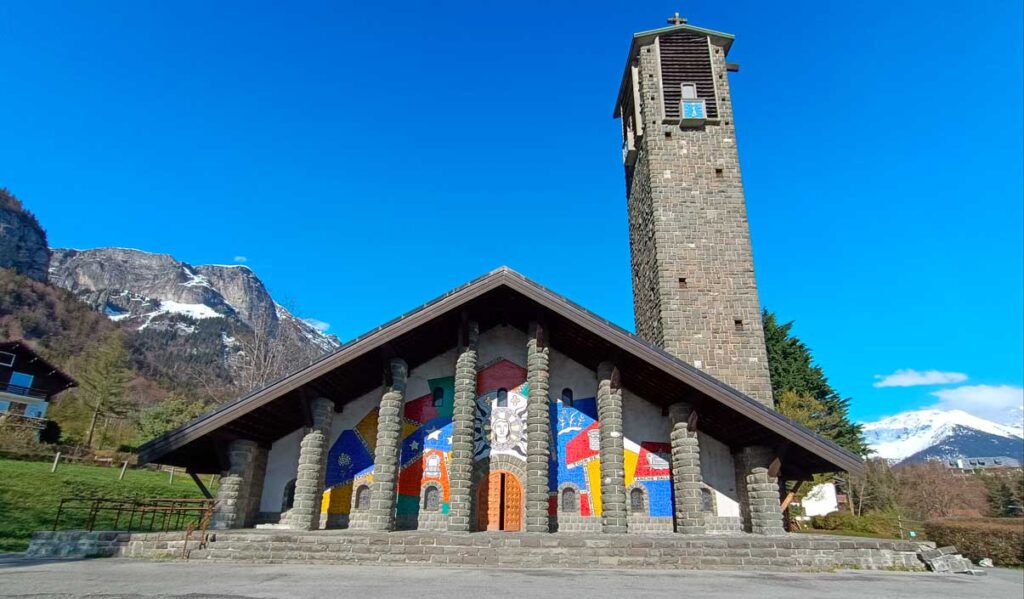 Façade de l'église de Passy vue dans sa totalité, avec sa mosaïque monumentale, sur fond de ciel bleu et de montagnes enneigées