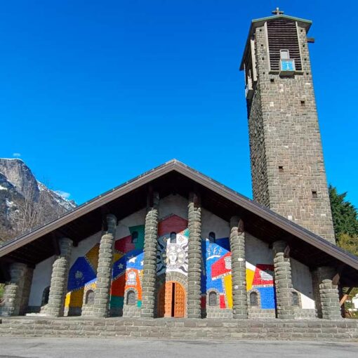 Façade de l'église de Passy vue dans sa totalité, avec sa mosaïque monumentale, sur fond de ciel bleu et de montagnes enneigées
